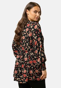 Blusa nera con motivi floreali rossi e bianchi. Maniche lunghe e vita aderente, con dettagli plissettati per aggiungere texture.