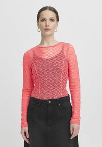 Top in pizzo a maniche lunghe di un vivace colore rosa con un motivo floreale e un design aderente, abbinato a una gonna nera a vita alta.