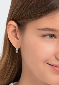 Zilveren ringoorbel met een vlinderhanger met roze accenten. Close-up toont de gladde metaalstructuur en het ingewikkelde ontwerp van de hanger.