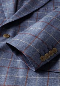 Modrý károvaný rukáv saka so štyrmi hnedými gombíkmi a jemným červeno-bielym mriežkovým vzorom na textúrovanom materiáli.