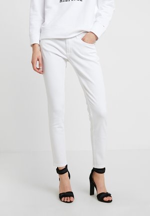 Jeans skinny de mezcla de algodón blanca combinados con un sudadera blanca con letras marinas, complementados con sandalias de tacón negro.