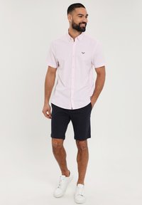 Lichtroze kortebloushirt met knopen en geborduurd logo, gecombineerd met marineblauwe shorts en witte sneakers. Gladde stoftextuur.