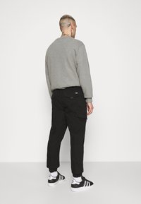 Šedá mikina v kombinaci s černými cargo kalhotami s kapsami. Model nosí černobílé tenisky s žebrovanými manžetami. Minimalistický design.