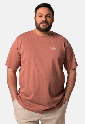 Camiseta de color óxido hecha de un tejido suave, con mangas cortas y un cuello redondo, que presenta un pequeño logotipo bordado en el pecho.