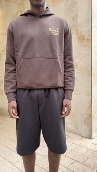 Sweatshirt capuz castanho com bolso frontal e logotipo, combinado com calções cinza-escuro. Ambos feitos de um tecido suave e texturado.