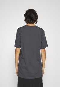 Camiseta de algodón gris con mangas cortas y cuello redondo, que presenta un ajuste relajado y holgado y un diseño simple. Sin gráficos ni patrones visibles.