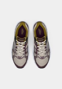 Chaussures de course Saucony en mesh beige clair avec des accents violets foncés et jaunes. Présentent des lacets blancs et une semelle rembourrée.