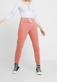 Rosa mjukisbyxor med elastisk midja och dragsko, sidofickor. Ribbad långärmad tröja i ljusblått. Svarta höga sneakers.