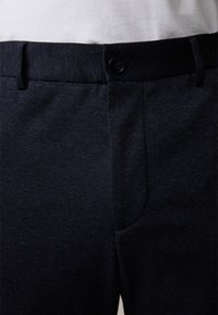Granatowe spodnie z teksturowanej tkaniny, wyposażone w zapięcie na guzik, boczne kieszenie oraz dopasowany krój.