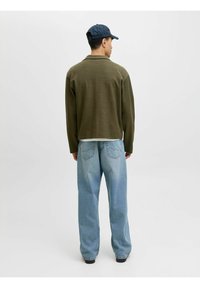 Pull en maille vert olive et jean pagne bleu clair. Le pull a un col, une coupe décontractée avec une texture. Casquette noire portée.