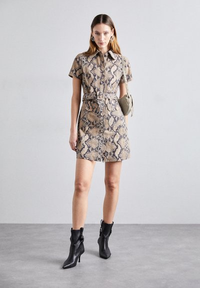 Robe à manches courtes avec un motif python beige et brun foncé, présentant un devant à boutons et une taille ceinturée. Portée avec des bottines noires.