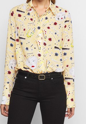 Yellow button-up shirt with abstract faces, musical instruments, notes, and red and blue starbursts worn with black pants and belt.