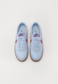 Lysblå sneakers med en glat overflade, røde accenter og en brun gummisål. Funktioner inkluderer snørebånd og et logo på tungen.