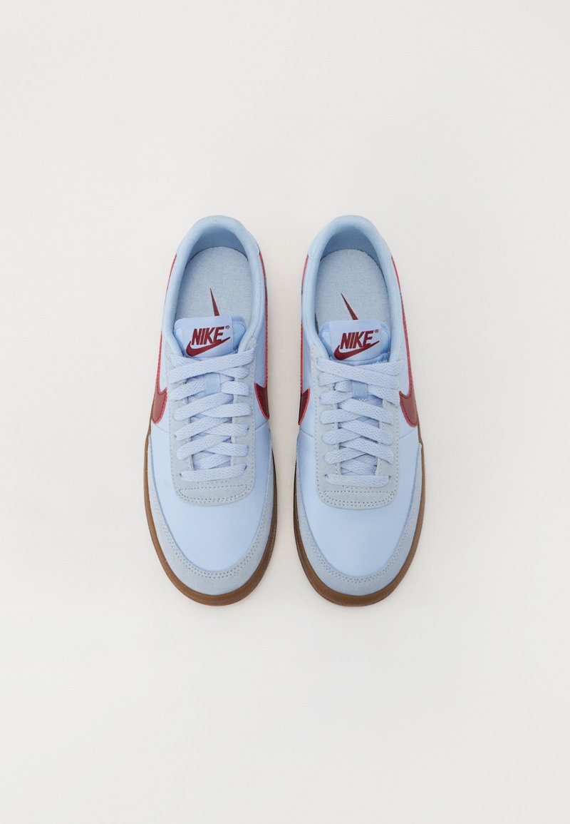Lichtblauwe sneakers met een gladde afwerking, rode accenten en een bruine rubberen zool. Kenmerken zijn onder andere veters en een logo op de tong.