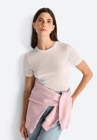 Striped short-sleeve T-shirt in light beige and white, paired with a pink sweatshirt tied around the waist, set against a plain background.
