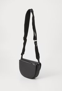 Borsa a tracolla nera a forma di mezzaluna con tasca frontale con cerniera e tracolla regolabile in tessuto largo su sfondo bianco.