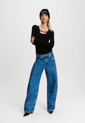 Black ribbed long-sleeve top with scoop neckline, high-waisted blue wide-leg jeans, complemented by a black knit beanie featuring logo text.