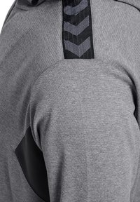 Grauer Sportsweatshirt mit strukturiertem Stoff, schwarzen Akzenten und einem gemusterten Streifen an der Schulter mit Zickzack-Designs.