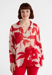 Blouse rouge à fleurs avec col, manches longues et coupe ample. Tissu transparent avec un fond clair et un motif de roses rouges.