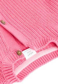 Pink knitted baby sweater with a ribbed texture, featuring wooden buttons, a soft neckline, and a label displaying "NEXT Baby."