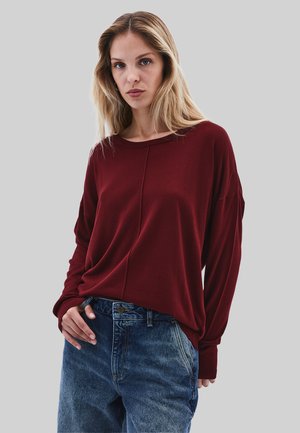 Top a maniche lunghe bordeaux con vestibilità rilassata, scollo a girocollo e polsini a costine, abbinato a jeans in denim blu a vita alta.
