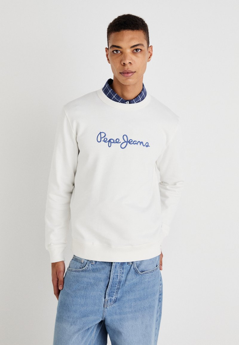 Sudadera blanca con bordado azul de la marca "Pepe Jeans", cuello redondo, puños y dobladillo acanalados, llevada sobre una camisa de cuadros azul.