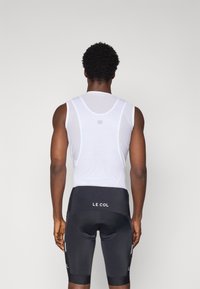 Couche de base sans manches blanche en mesh et shorts de cyclisme noirs avec rembourrage. Présente un logo sur les shorts et une coupe ajustée pour le cyclisme.