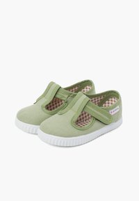 Zapatos de lona verdes con una correa segura y un forro de patrón de espiga. Suelas de goma con bordes blancos texturizados para mayor agarre.