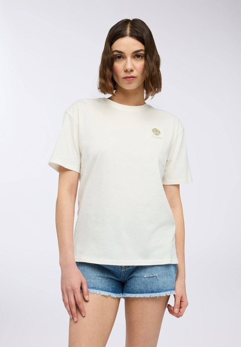 T-shirt in cotone color crema con scollo rotondo e maniche corte. Presenta una piccola grafica di conchiglia verde nella zona sinistra del petto.