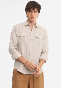 Camicia button-up beige chiaro con un motivo testurizzato, due tasche sul petto e maniche arrotolate, realizzata in un tessuto leggero.