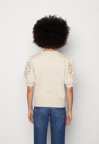 Pletený svetr v krémové barvě s nafouklými rukávy a výšivkou s dírkovými vzory. Má kulatý výstřih a přiléhavý spodní lem. Nosený s modrými džíny.