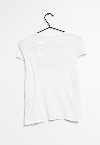 Vit kortärmad t-shirt hängande på en svart klädhängare, med rund halsringning och ett mjukt, lätt tyg.