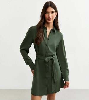 Long-sleeve, button-up dress in dark green fabric. Features a tied belt at the waist, smooth texture, and a collar for a structured look.