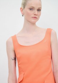Korálové šaty s lodičkovým výstřihem vyrobené z hladké látky, s minimalistickým designem, postranními kapsami a bez viditelných vzorů nebo akcentů.