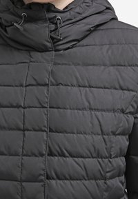 Black quilted puffer jacket with a high collar, adjustable drawstring hood, and smooth texture. Features horizontal stitching and zipper closure.