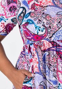 Vestido de colores con estampado de grandes motivos paisley en rosa, azul y negro. Mangas cortas y cintura fruncida con un bolsillo lateral.