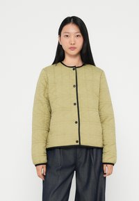 Vatteret, lys olivengrøn jakke med sort kant og knapper. Designet har et diamantmønster og lange ærmer.