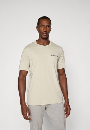 T-shirt en coton beige à manches courtes et col rond, avec un petit logo "Champion" noir sur la poitrine gauche.