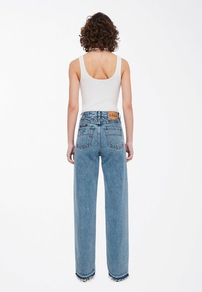 Jeans de tiro alto anchos de color azul claro con dobladillo deshilachado. Presenta una etiqueta de la marca visible y bolsillos traseros, combinados con una camiseta ajustada blanca.