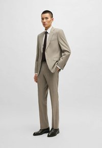Completo a quadri beige con vestibilità su misura, rever slim e una tasca sul petto. Abbinato a una camicia bianca e cravatta marrone scuro, scarpe nere.