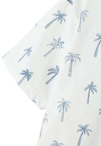 Chemise à manches courtes en tissu blanc avec un motif de palmiers bleus. Le matériau semble doux, avec une texture lisse et des coutures soignées.