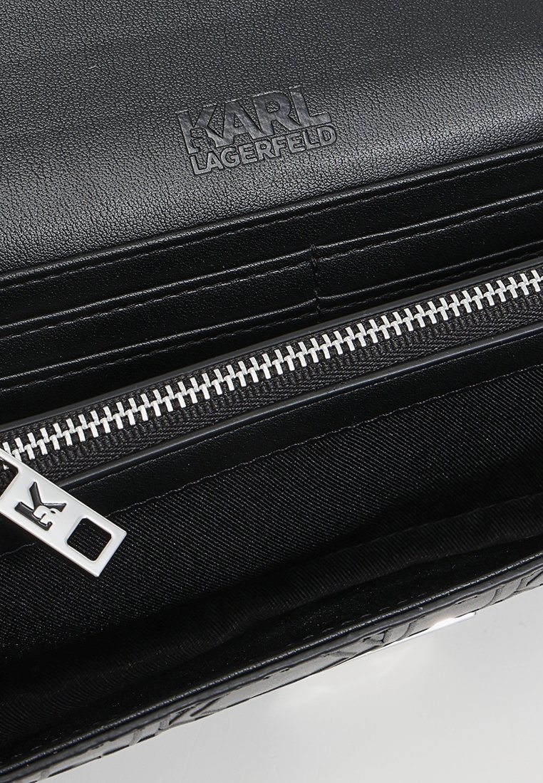 Intérieur d'un portefeuille en cuir noir Karl Lagerfeld avec une fermeture éclair argentée et un logo de la marque embossé au-dessus des emplacements pour cartes.