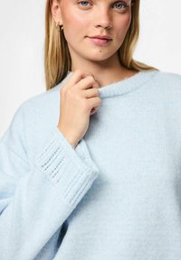 Jasnoniebieski sweter wykonany z miękkiego dzianinowego materiału z prążkowanymi mankietami i dekoltem. Posiada luźny krój i subtelną teksturę.