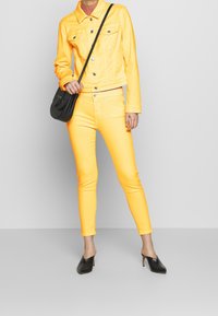 Gul denimjacka och matchande skinny jeans, båda gjorda av ett mjukt material, med svarta mules och en liten svart axelväska.