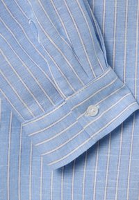 Tessuto di camicia a righe azzurro chiaro, con sottili righe bianche e blu scuro, dotato di polsino abbottonato e una trama visibile e textured.