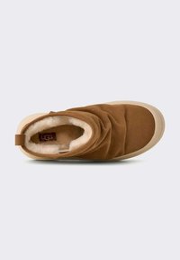 Scarpa slip-on in suede marrone con una morbida fodera color crema, caratterizzata da un design arricciato e suola in gomma beige. Logo UGG visibile all'interno.