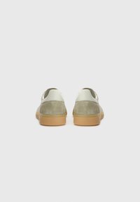 Grüne Wildledersneaker mit einem weißen Leder-Fersenpatch und einer strukturierten Gummisohle. Mit sichtbaren Nähten und einem Low-Top-Design.