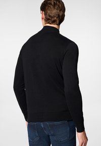 Czarny sweter z długimi rękawami i prążkowanym kołnierzem. Wykonany z dzianiny, dopasowany krój, bezszwowy tył, noszony z niebieskimi dżinsami.