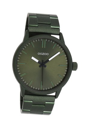 Montre analogique verte avec une finition mate, un cadran rond, des marqueurs d'heure blancs et des aiguilles, bracelet en métal et une bande texturée.