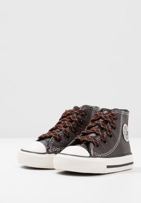 Czarne buty wysokie z teksturowanej skóry, biała gumowa osłona palców, pomarańczowe sznurowadła i okrąła łatka z logo po boku.